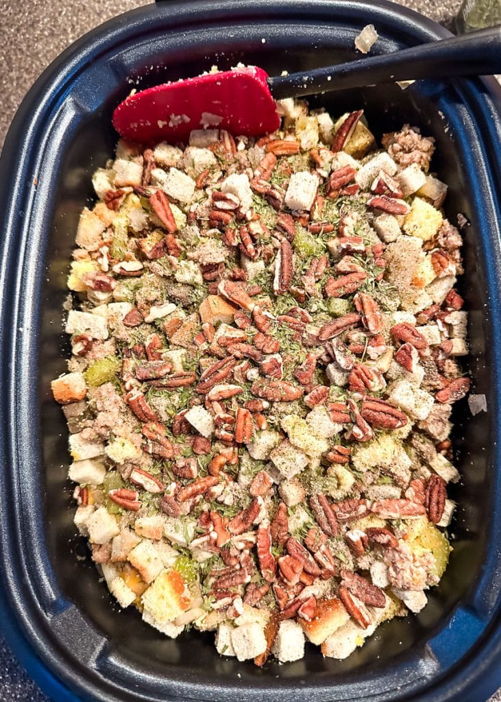 All stuffing ingredients added to the slow cooker, including spices, herbs and pecans.