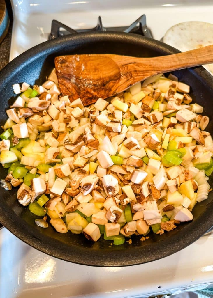 Mushrooms, diced apples, onion and celery being sauteed in a skillet.