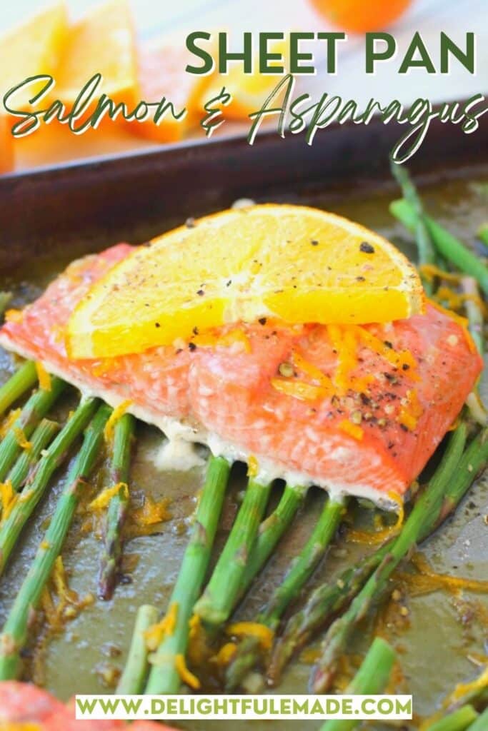 Salmon filet topped with slice of orange and on a pan of asparagus.