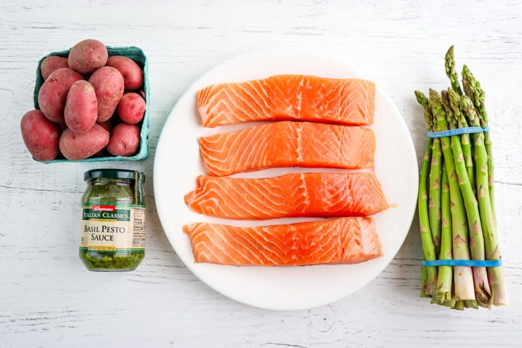 Fresh uncooked salmon filets with baby red potatoes, a jar of pesto and asparagus spears.