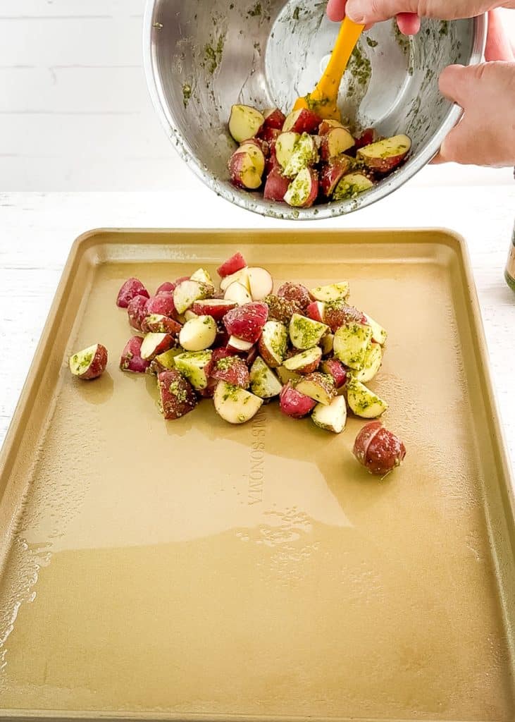 Pesto coated potatoes being poured onto a sheet pan to be roasted.