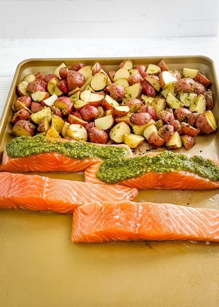 Salmon filets on the pan with the potatoes and pesto sauce on top of the filets.