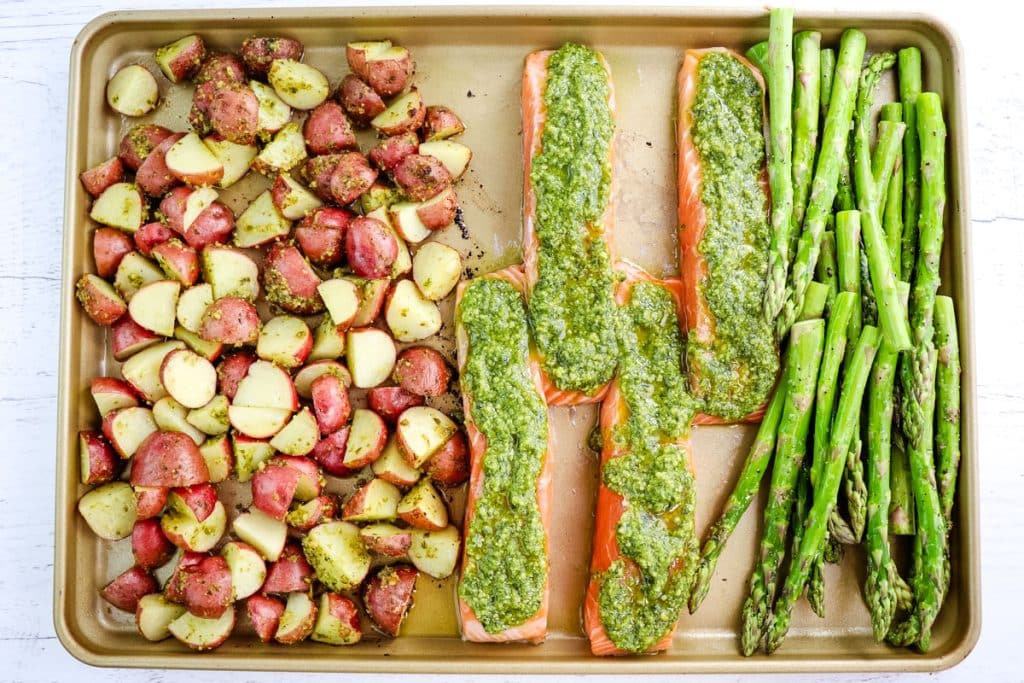 Potatoes, salmon with pesto sauce and asparagus spears on a sheet pan before going into the oven.