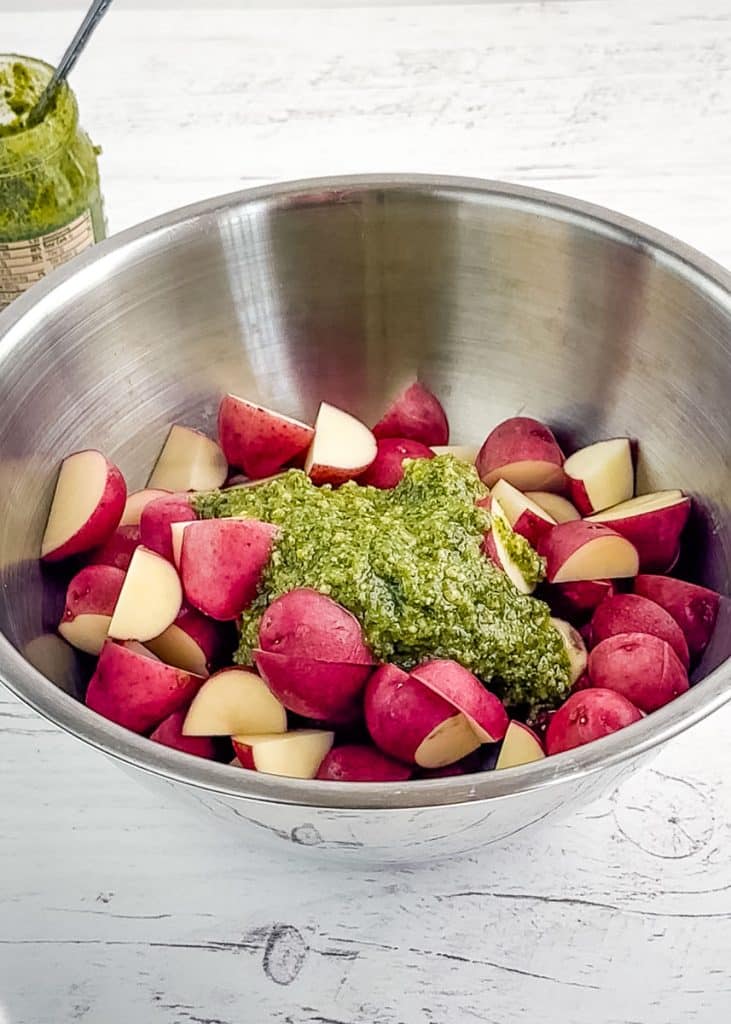 Quartered red potatoes in a mixing bowl with pesto sauce.