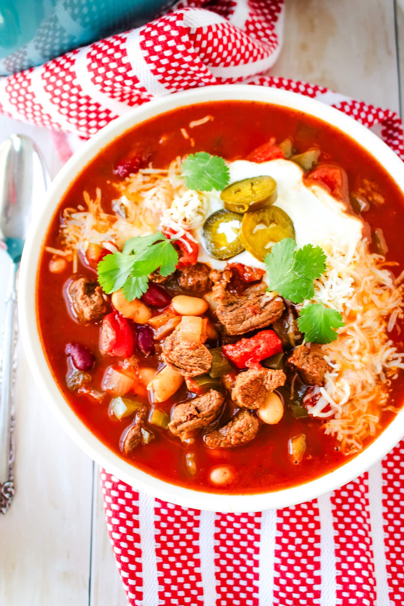 Chipotle steak chili recipe topped with shredded cheese, sour cream, cilantro and sliced jalepenos.