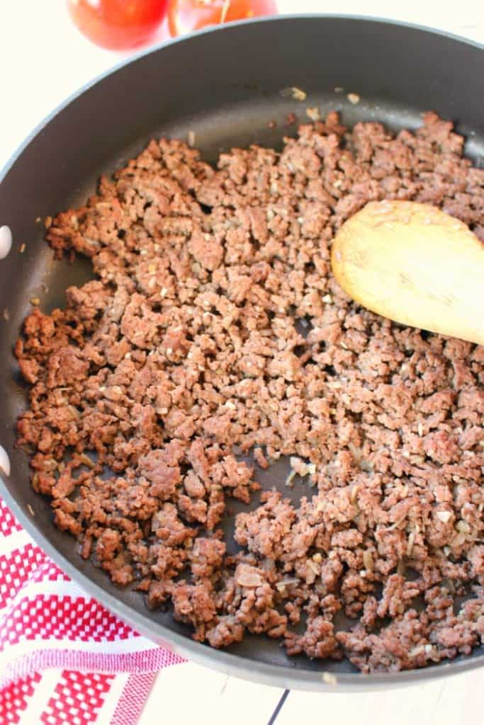 Grould beef that has been browned in a skillet with a wooden spoon.