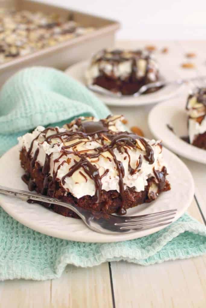 Almond joy poke cake slice on a plate drizzled with hot fudge sauce with fork on the plate.