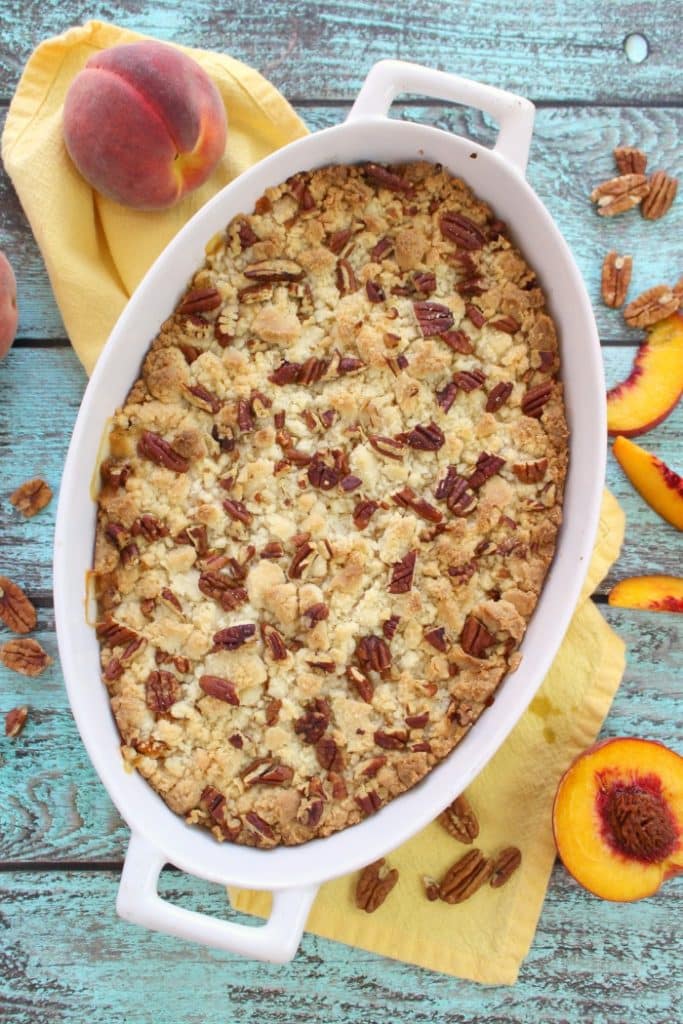 Peach cobbler dump cake baked in baking dish with fresh peaches on the side.