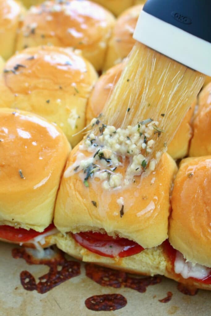 Pepperoni pizza sliders being brushed with garlic butter.