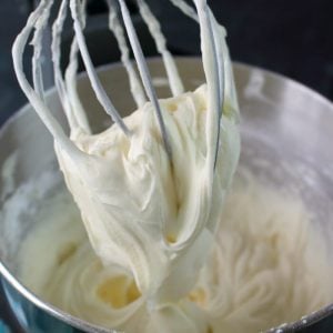 Cream cheese frosting in a mixing bowl with a whisk attachment holding the frosting.