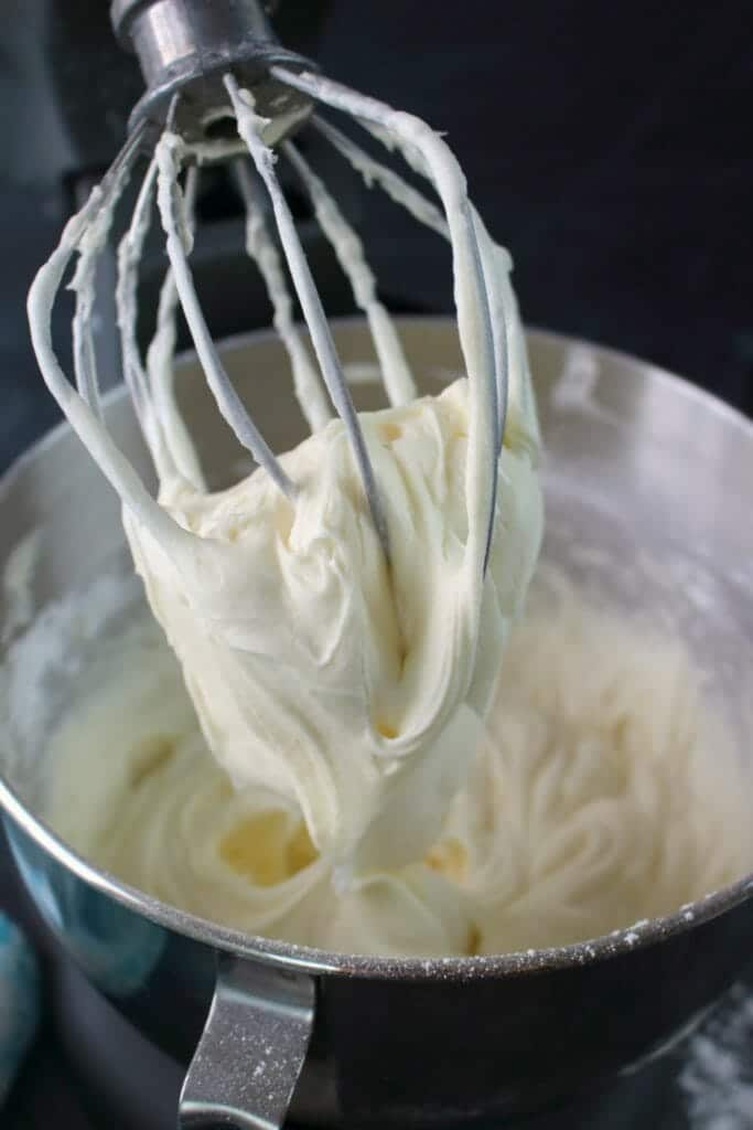 Cream cheese frosting in a mixing bowl with a whisk attachment holding the frosting.