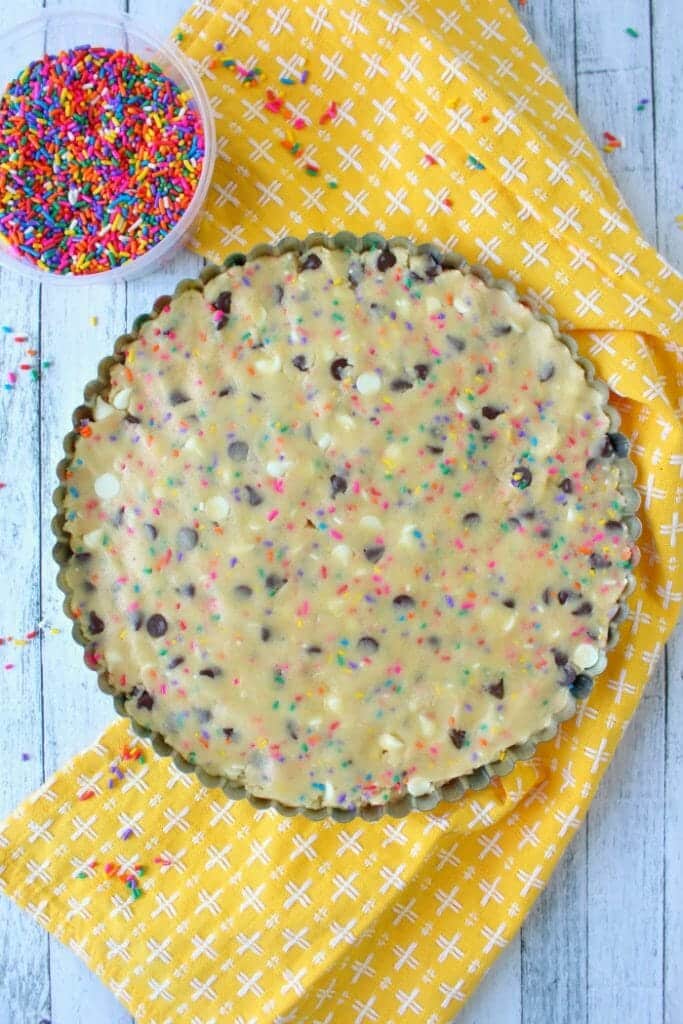 This Funfetti Giant Chocolate Chip Cookie Cake has party written all over it! Make with lots of rainbow sprinkles, white and semi-sweet chocolate chips and topped with a delicious buttercream frosting, this giant cookie is perfect for a birthday party or celebration!