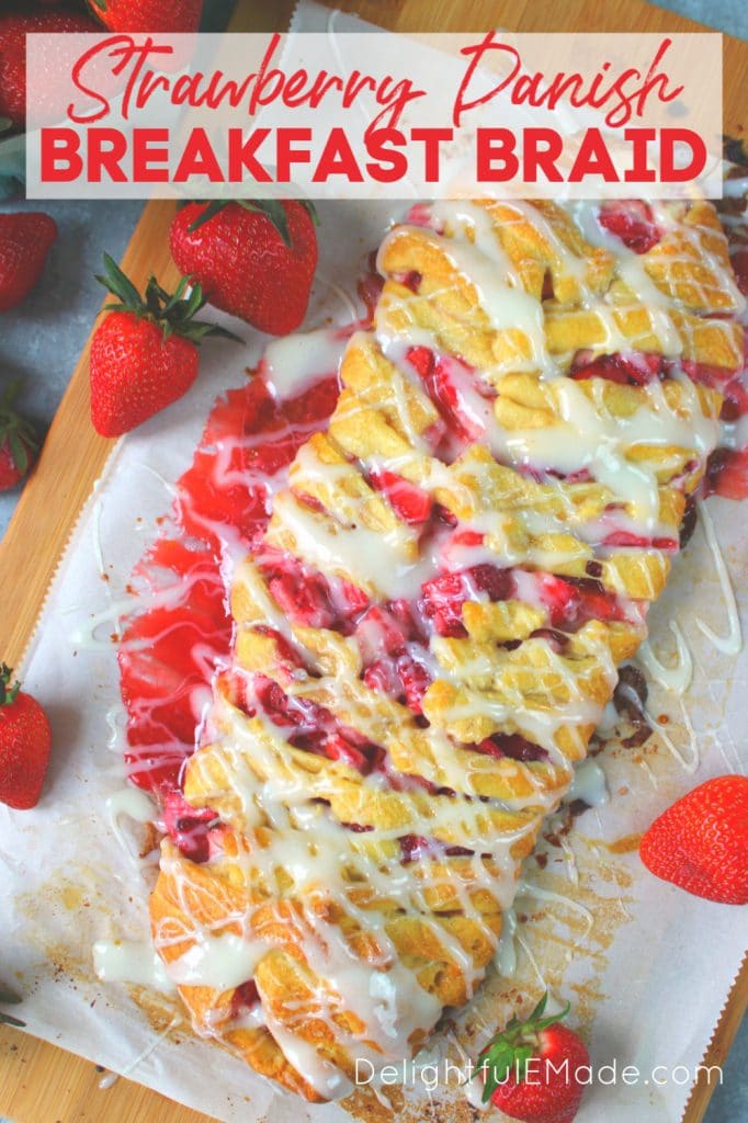 Strawberry danish braid on wooden cutting board with frosting drizzle and fresh strawberries.