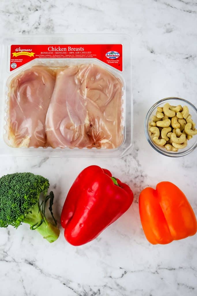 Cashew chicken ingredients, including chicken breasts, broccoli, bell peppers and cashews.