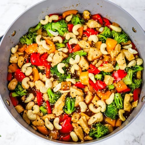 Cashew chicken stir fry recipe in a large skillet topped with whole cashews and sesame seeds.