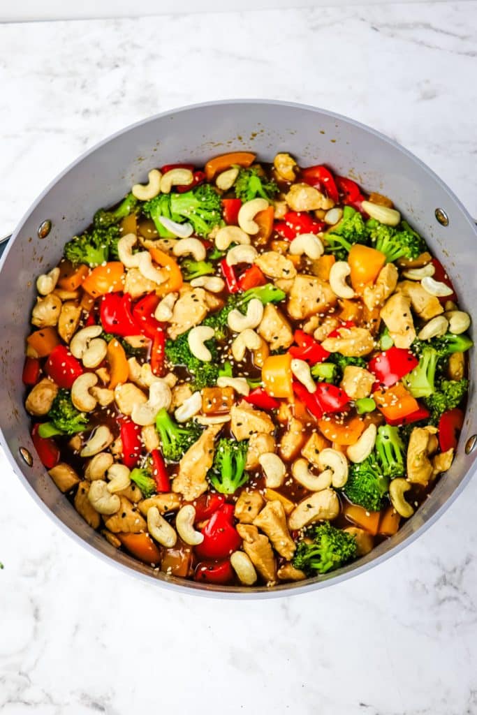 Cashew chicken stir fry recipe in a large skillet topped with whole cashews and sesame seeds.