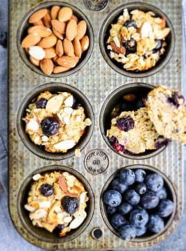 Blueberry protein muffins in a muffin tin with whole almonds and fresh blueberries on the side.