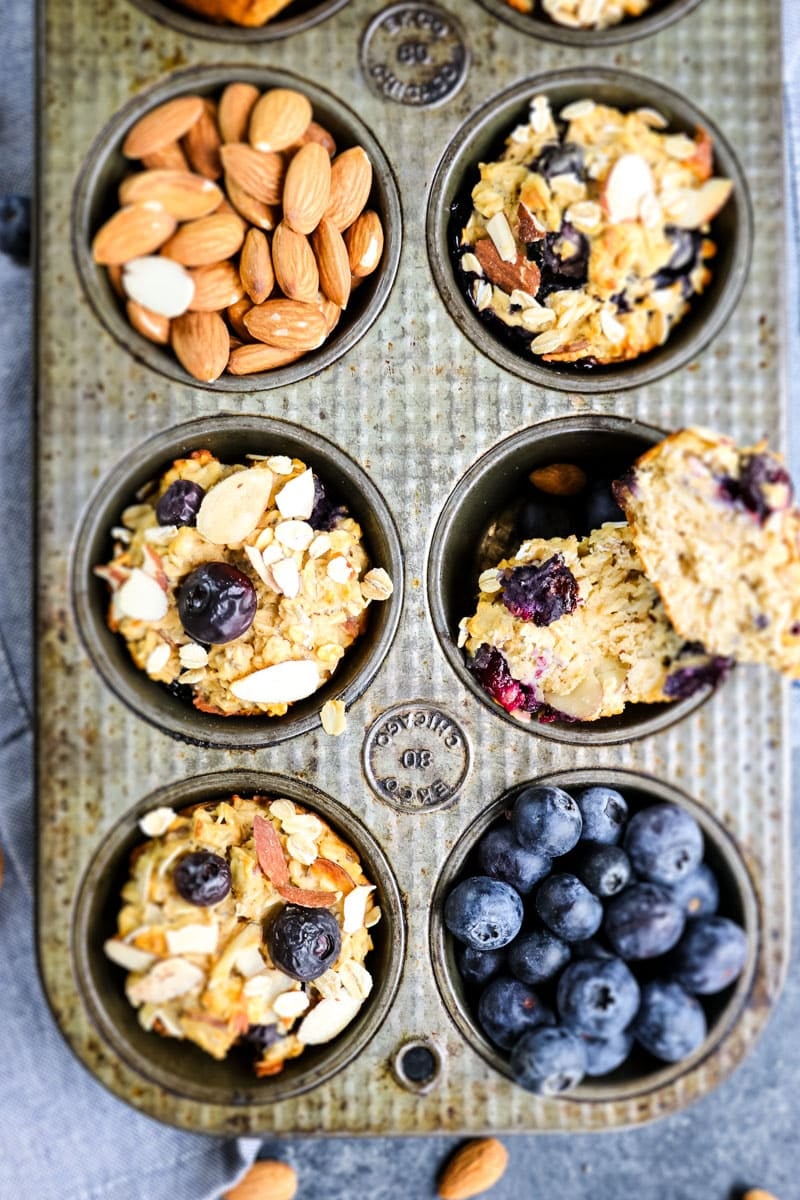 Blueberry protein muffins in a muffin tin with whole almonds and fresh blueberries on the side.