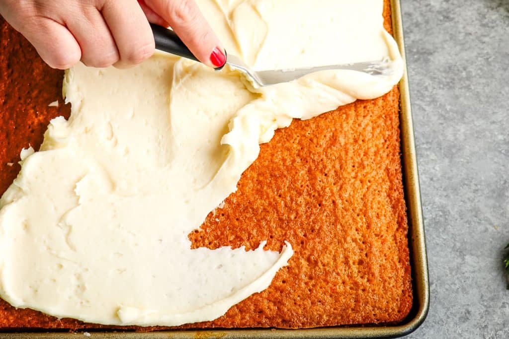 Carrot sheet cake being frosted with cream cheese frosting.