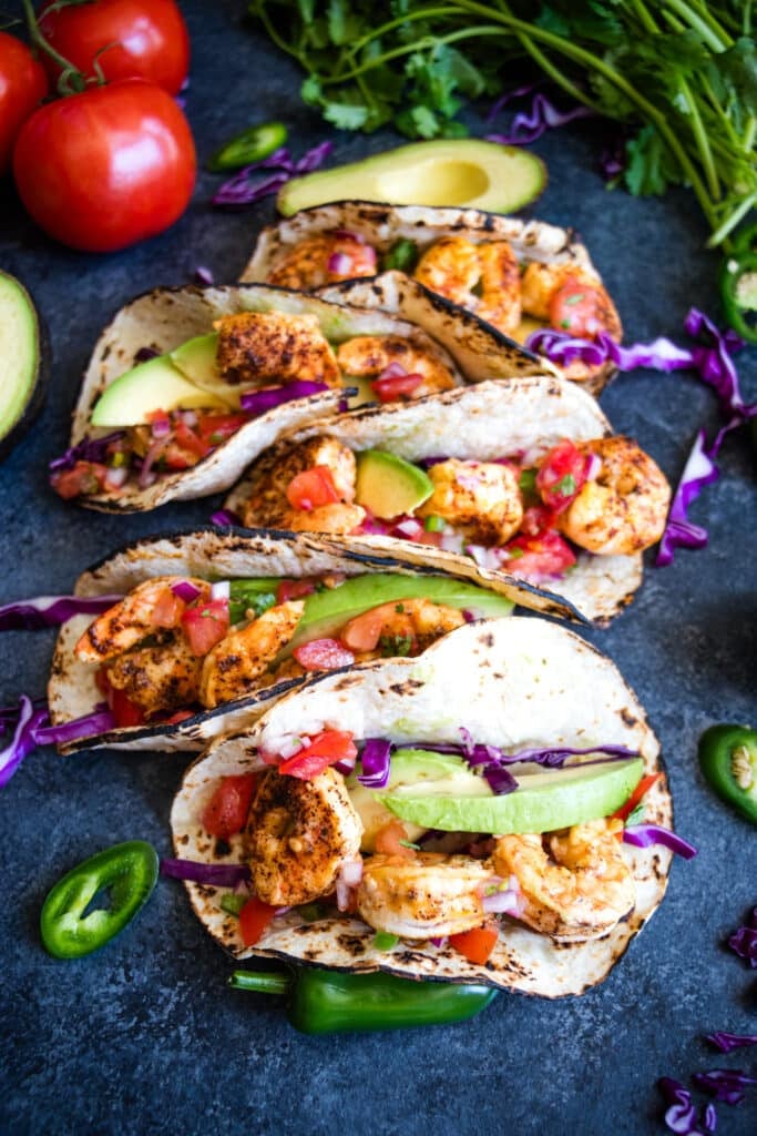 Five air fryer shrimp tacos served with avocado, tomato, cilantro, jalapenos and red cabbage.