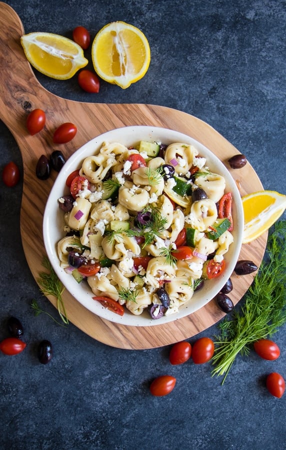 Greek tortellini pasta salad in bowl, garnished with lemons, tomatoes and dill.