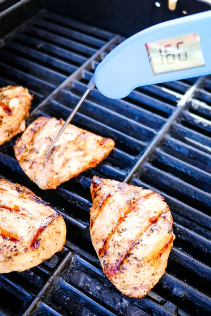 Italian grilled chicken breasts on the grill with digital thermometer taking internal temperature.