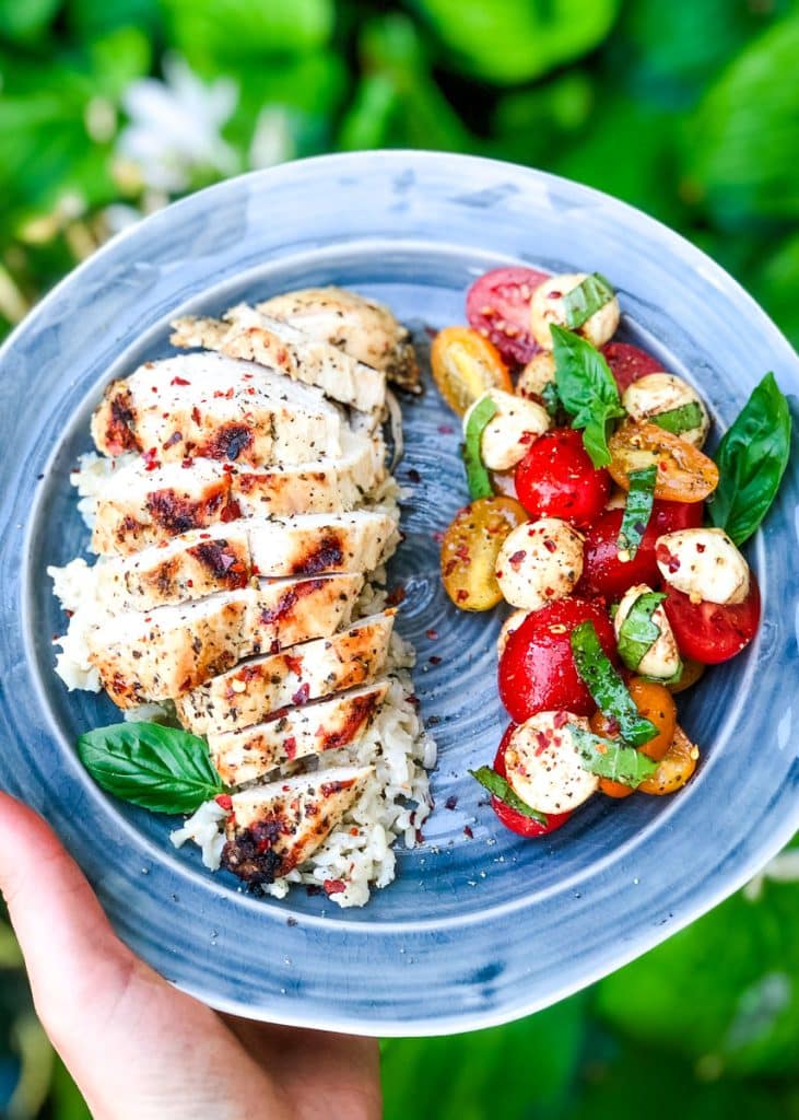Sliced Italian grilled chicken on a plate served with tomato, basil and mozzarella salad.