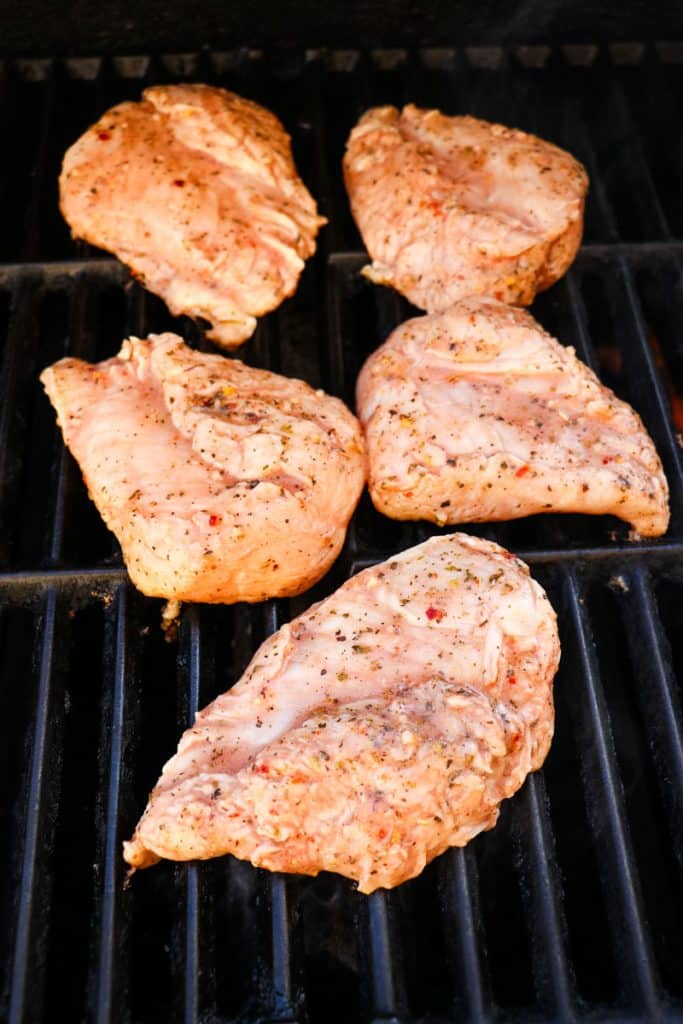 Italian marinated chicken breasts on grill grates being cooked.