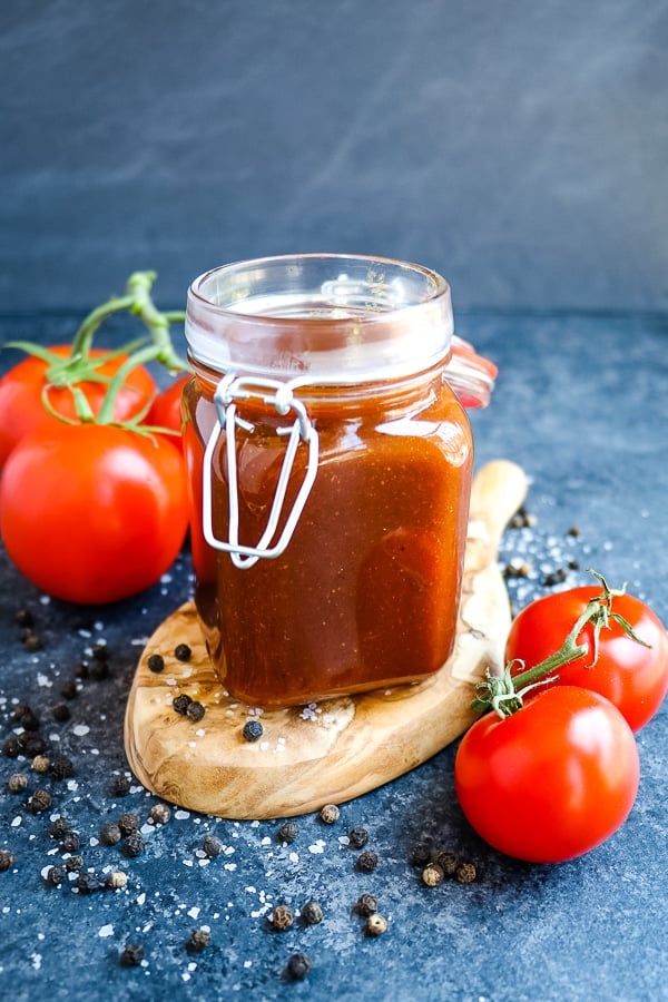 Homemade honey bbq sauce in a small jar with tomatoes on the side.
