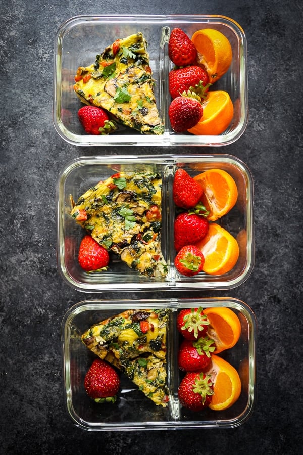 Baked spinach and veggie frittata in meal prep containers with fruit.