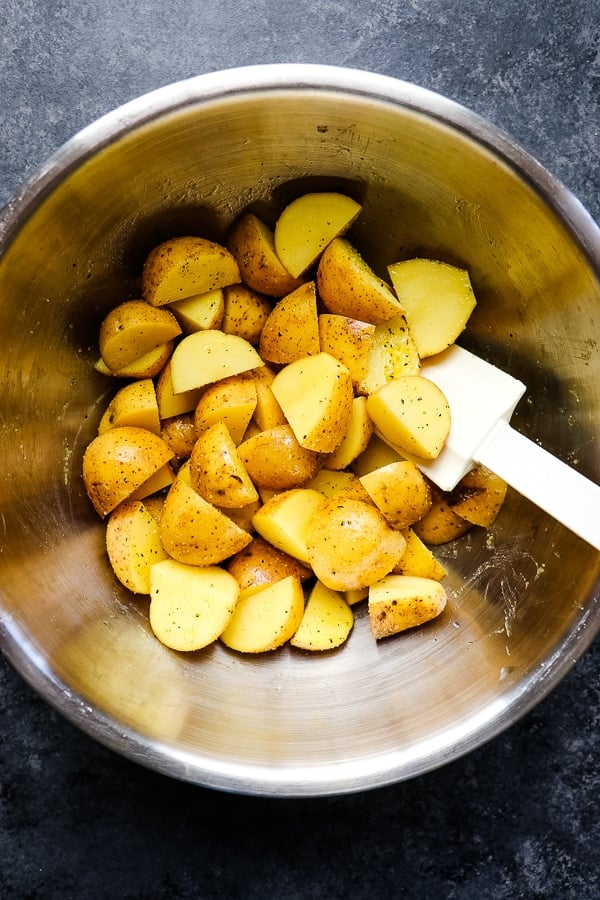 Yellow potatoes in a mixing bowl that have been cut, oiled and seasoned.