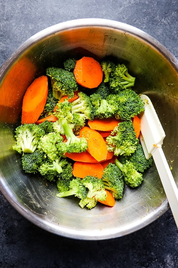 Sliced carrots and broccoli florets in a mixing bowl with a spatula.