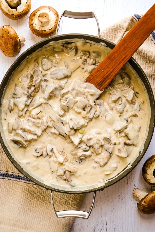 Skillet with completed classic beef stroganoff in sour cream sauce, with wooden spoon off to side.