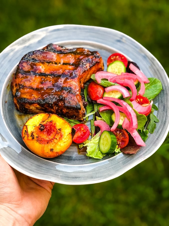 Plate of food with grilled pork chop, grilled peach and side salad with pickled red onions.