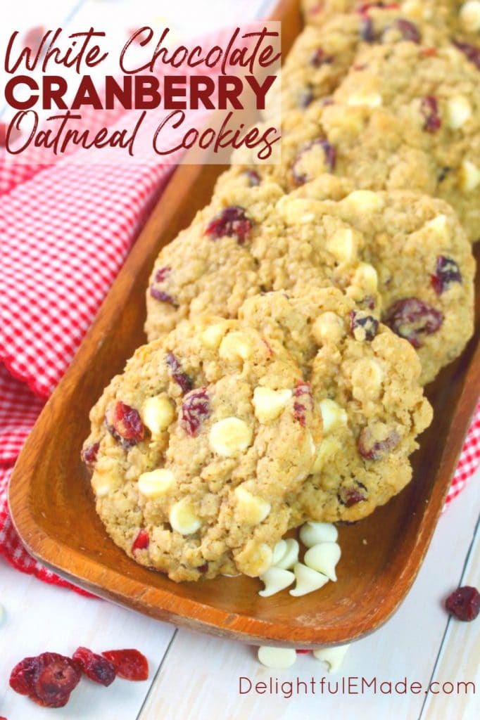 White chocolate cranberry oatmeal cookies on a wooden platter with extra cranberries and white chocolate chips.