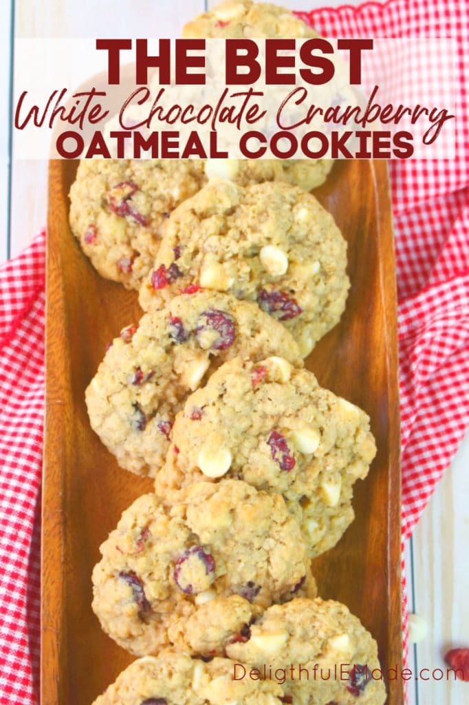 White chocolate cranberry oatmeal cookies on a wooden platter with extra cranberries and white chocolate chips as a garnish.