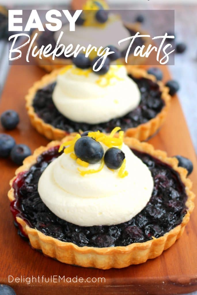 Single serving blueberry tarts on a serving board, topped with lemon mascarpone cream, and fresh blueberries and lemon zest as a garnish.