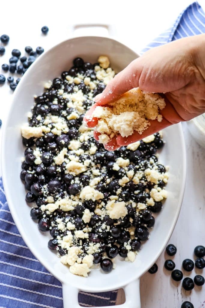 Cake mix crumble being added to the blueberries in the baking dish.