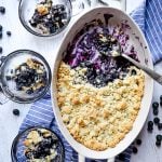 Blueberry cobbler dump cake in oval baking dish with three bowls of cobbler on the side.