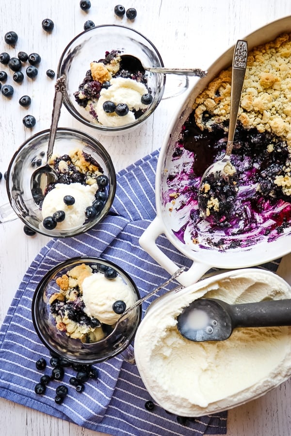 Blueberry dump cake in baking dish with container of vanilla ice cream and individual servings with scoops of vanilla ice cream.