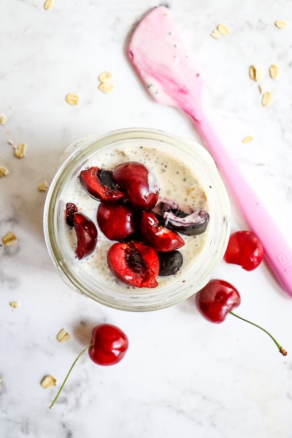 Overhead shot of overnight oats in mason jar, with fresh pitted, cherry halves on top.