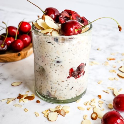 Cherry overnight oats with sliced almonds and pitted cherries on top. Whole, fresh cherries garnished on the side.