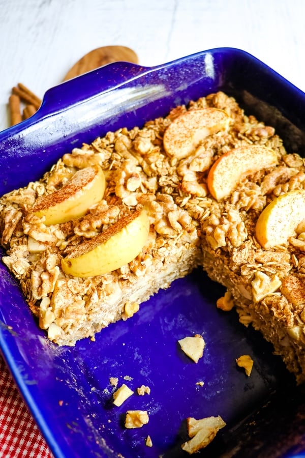 Baking dish with apple cinnamon baked oatmeal topped with apple slices, walnuts and sprinkle of cinnamon.
