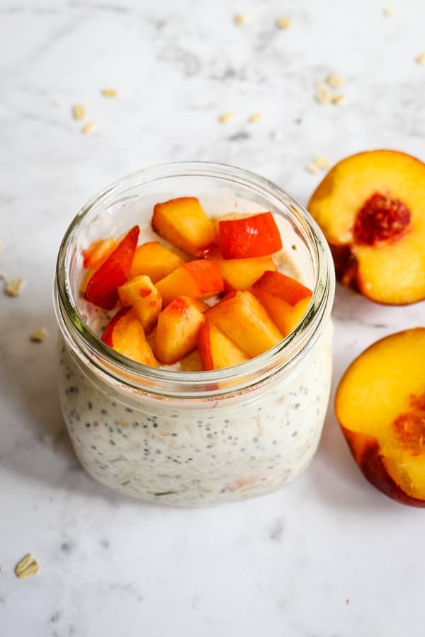 Overnight oats topped with peach chunks, garnished with whole peaches on the side.