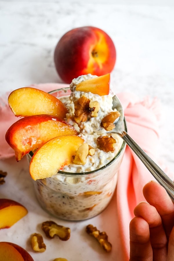 Cup of peach overnight oats, taking out spoonful of oats with peach chunks.