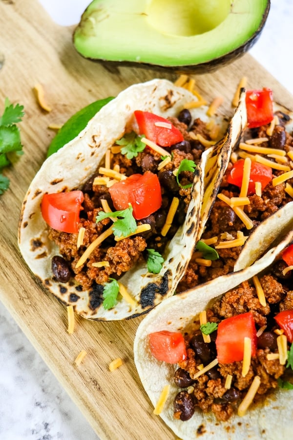Ground beef tacos on board with tomatoes, cilantro and cheese.