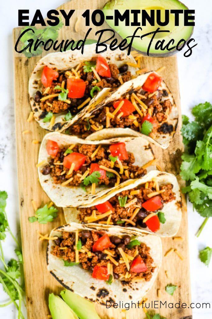 Ground beef tacos on board garnished with cilantro, limes and avocado slices.