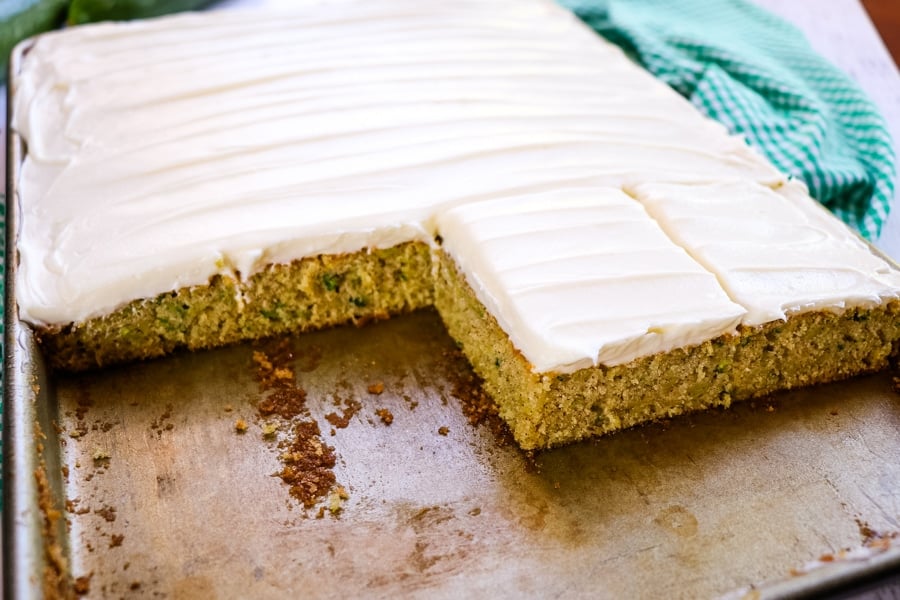 Zucchini cake with cream cheese frosting, sliced into squares in sheet pan.