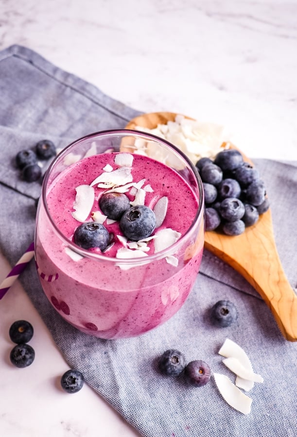 Healthy blueberry protein smoothie in a glass topped with blueberries and coconut.