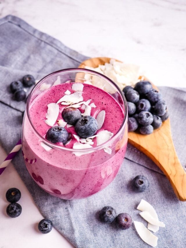Healthy blueberry protein smoothie in a glass topped with blueberries and coconut.